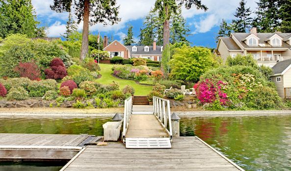 Brick red house with English garden and white window shutters. Summer landscape.