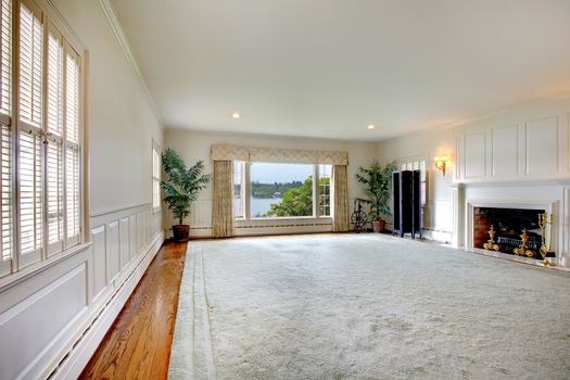 Large empty living room with huge rug, fireplace and lake view.