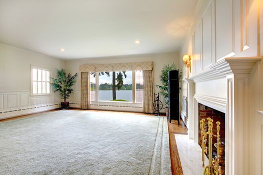 Large empty historical old living room interior with fireplace and lake view.