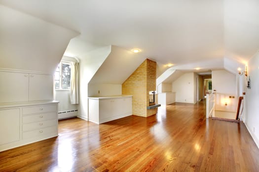 Large long attic room with fireplace. Empty with golden hardwood.