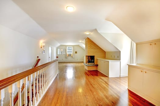 Large long attic room with fireplace. Empty with golden hardwood.