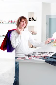 Young man at shopping mall checkout counter paying through credit card