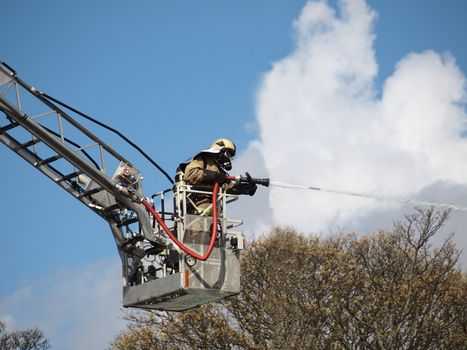 fireman on crane extinguishing fire above a burning building