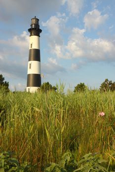 The Bodie Island lighthouse over marshes of the Cape Hatteras National Seashore on the Outer Banks of North Carolina against white clouds and a blue morning sky vertical