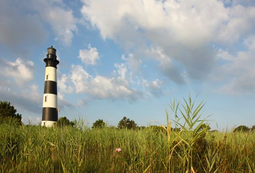 The Bodie Island lighthouse over marshes of the Cape Hatteras National Seashore on the Outer Banks of North Carolina against white clouds and a blue morning sky