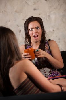 Shocked woman drinking coffee and sitting with friend