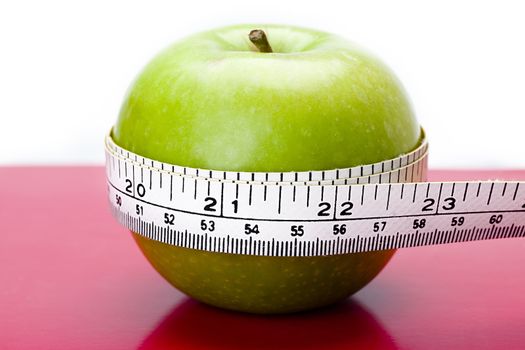 Shot of an apple on a table with a measuring tape around it.