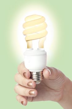 Close-up image of a hand holding a glowing fluorescent bulb isolated on a green background