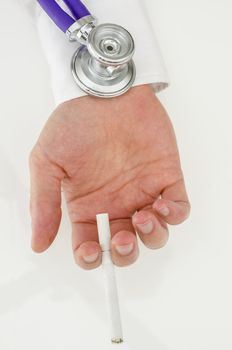 Stethoscope on a hand holding a cigarette on a white table.