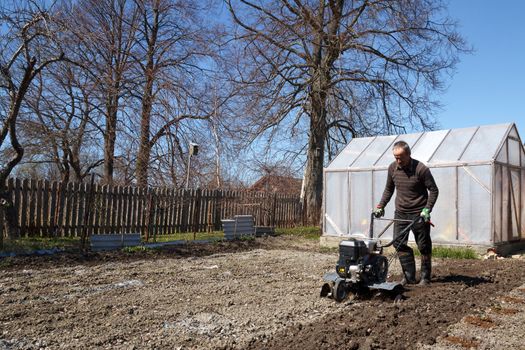 Middle age man with a rototiller in the garden 