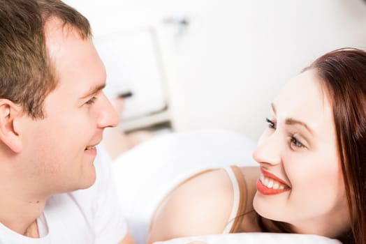 Young man and woman lying together in bed, smiling and happy