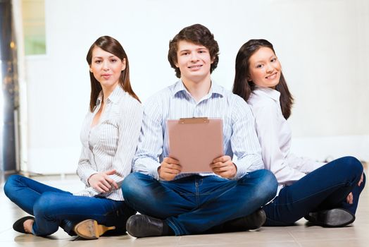 portrait of a group of young people sitting on the floor, man and two attractive women