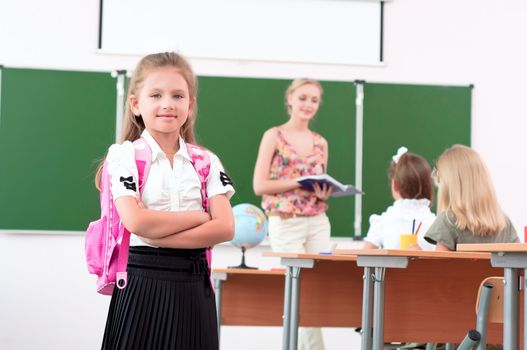 portrait of schoolgirl with a school backpack, in the background a classroom and the teacher tells the class