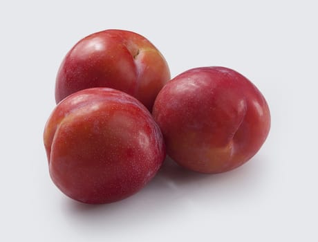 Three red plums on the grey background