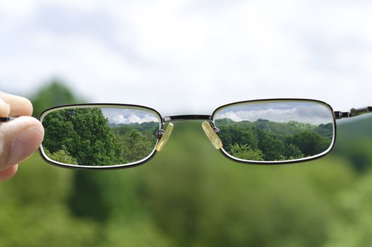 out of focus nature with hand holding a glasses that correct the vision