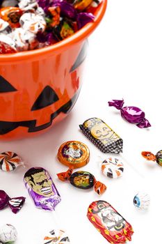 Halloween bucket with overflowing candies with some scattered on white floor.