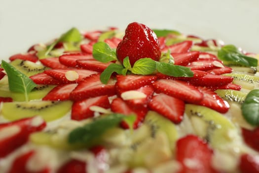 cake with cream filling covered with strawberries kiwi and mint green and almonds. close to