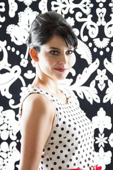 young woman in front of a black and white textured background with 60's inspired style with corner smile