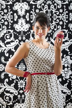 young woman is stylist 60's inspired clothing, holding up a velvet cupcake
