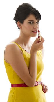 Young woman wearing a bring yellow dress looking at the camera while applying lipstick