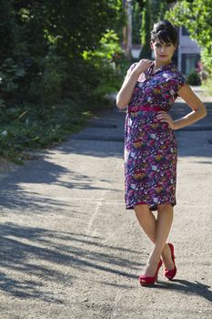 Young fashionable woman wearing a multi colored flower pattern dress posing in an urban alley