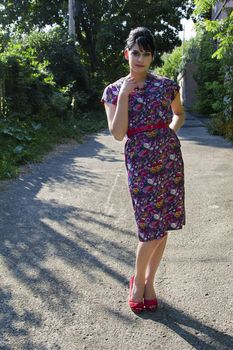 Young woman wearing a multi colored flower pattern dress posing in an urban alley