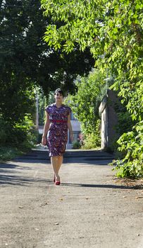 Young woman wearing a multi colored flower pattern dress walking in an urban alley