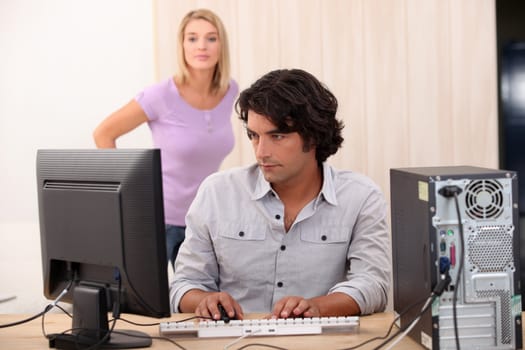 Male on his computer with his wife in the back.