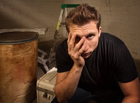 Unhappy young white man sitting on crate indoors