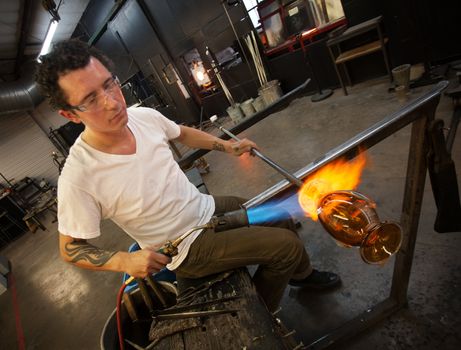 Adult male working in glass artist studio with blowtorch