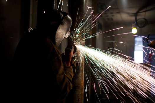 View of a welder cutting metal in protective workwear.