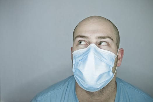 Young doctor with bald head wearing a mask and on a gray background (in studio)