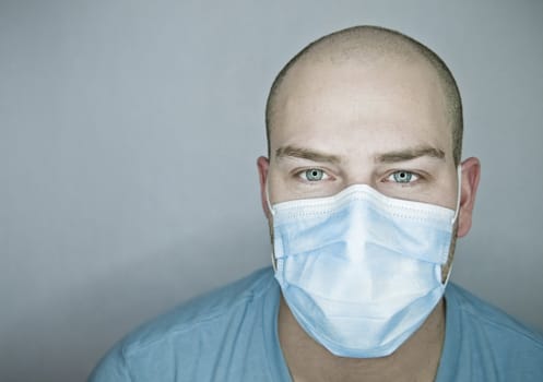 Young doctor with bald head wearing a mask and on a gray background (in studio)