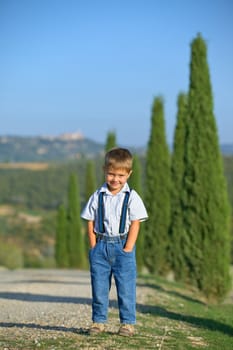 Cute boy having fun on vacations in Tuscan against cypress alley background. Vertical view