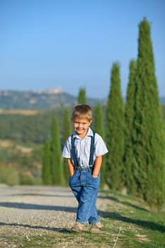 Cute boy having fun on vacations in Tuscan against cypress alley background. Vertical view