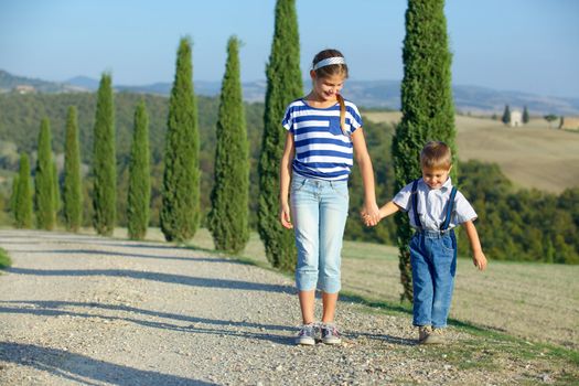 Happy sister and brother having fun on vacations in Tuscan against cypress alley background