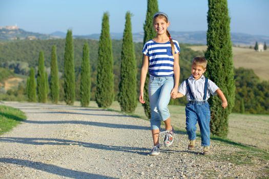 Happy sister and brother having fun on vacations in Tuscan against cypress alley background