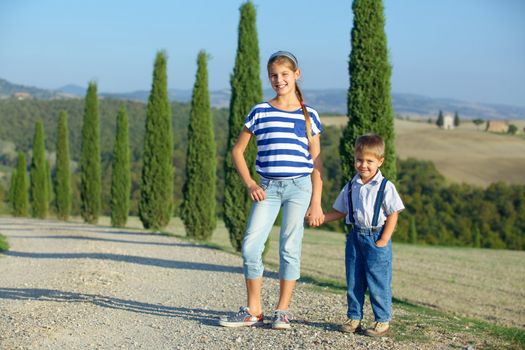 Happy sister and brother having fun on vacations in Tuscan against cypress alley background