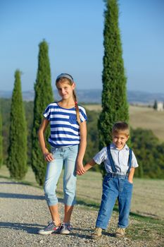 Happy sister and brother having fun on vacations in Tuscan against cypress alley background. Vertical view