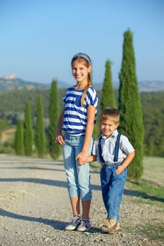 Happy sister and brother having fun on vacations in Tuscan against cypress alley background. Vertical view