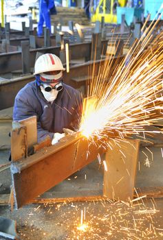 worker using torch cutter to cut through metal in factory