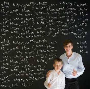 Thumbs up boy dressed up as business man with teacher man and chalk questions on blackboard background