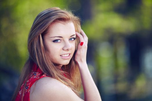 Beautiful woman in a red dress on a background of the spring woods and lakes