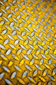Close up of real diamond plate material.  Most of the yellow paint is chipped and scratched off. Shallow depth of field.