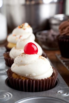 Close up of some decadent gourmet cupcakes frosted with a variety of icing flavors and toppings.