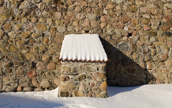 Vintage fort castle wall made of stone and small clay tile roof covered with snow in winter.