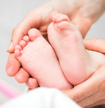 Mother's hands carefully keeping baby's feet with tenderness