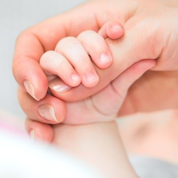 Close-up of baby's hand holding mother's finger with tenderness