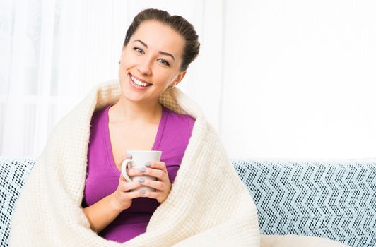 Young beautiful girl with tea cup in plaid on sofa