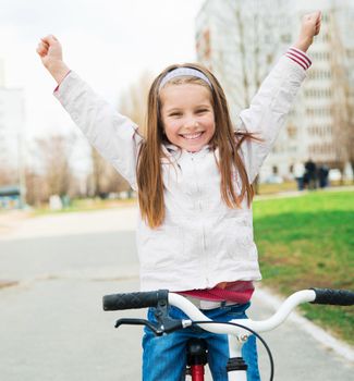 Portrait of a little girl on a bicycle with hands up